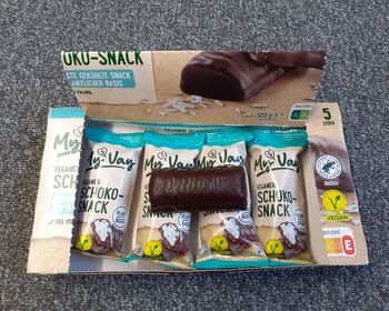 Box mit mehreren verpackten Schokoriegeln, ein ausgepackter Riegel liegt quer darüber.
