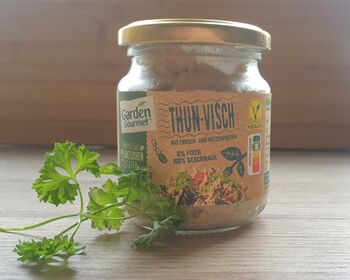 Ein Glas "ThunVisch" steht auf einer Holzfläche, davor ein Ästchen Petersilie.