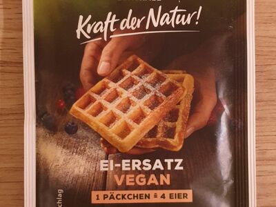 Vorderseite der Verpackung des Ei-Ersatzes von Bio-Zentrale. Hierauf abgebildet belgische Waffeln, die in der Hand gehalten werden.