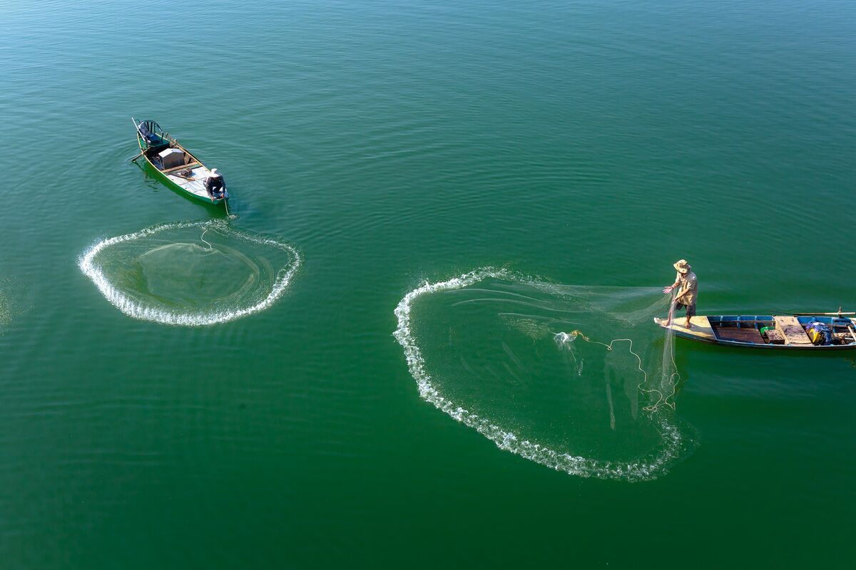 Zwei Fischer auf Booten werfen im blauen Meer ihre Netze aus.