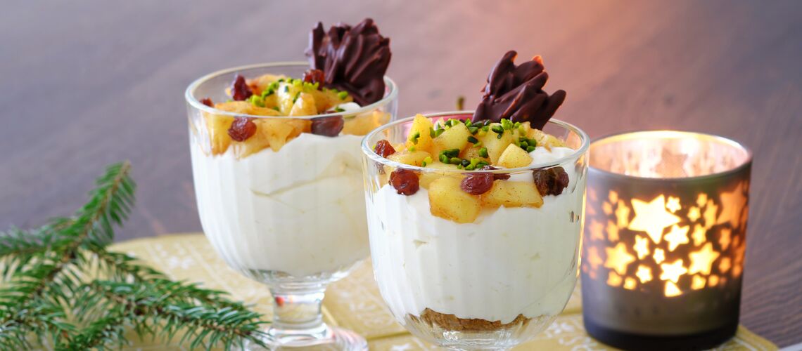 Zwei gefüllte Dessertschalen auf einer weihnachtlichen Serviette, die mit Tannenzweigen, Spekulatiuskeksen und einem Windlicht mit Sternenmuster dekoriert ist